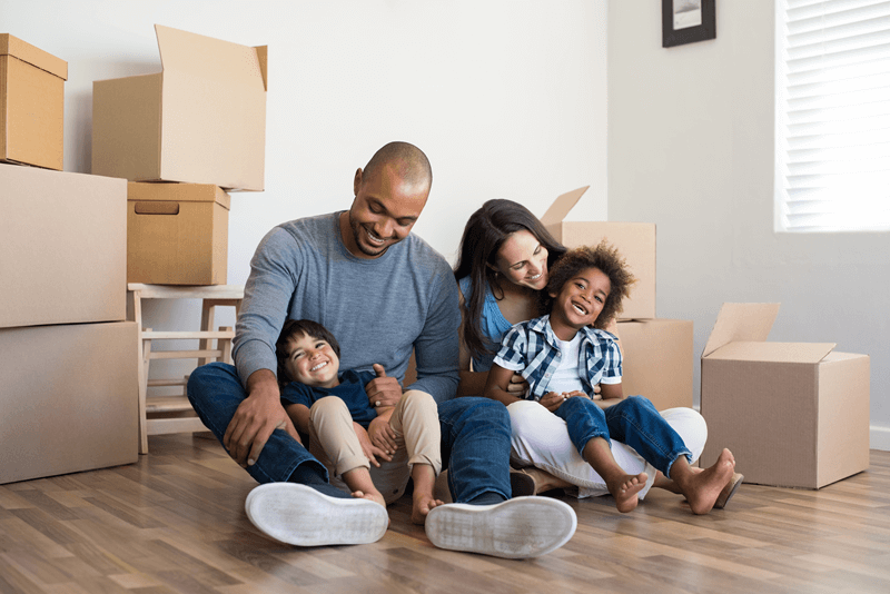 Family of 4 smiling on floor of new home with moving boxes